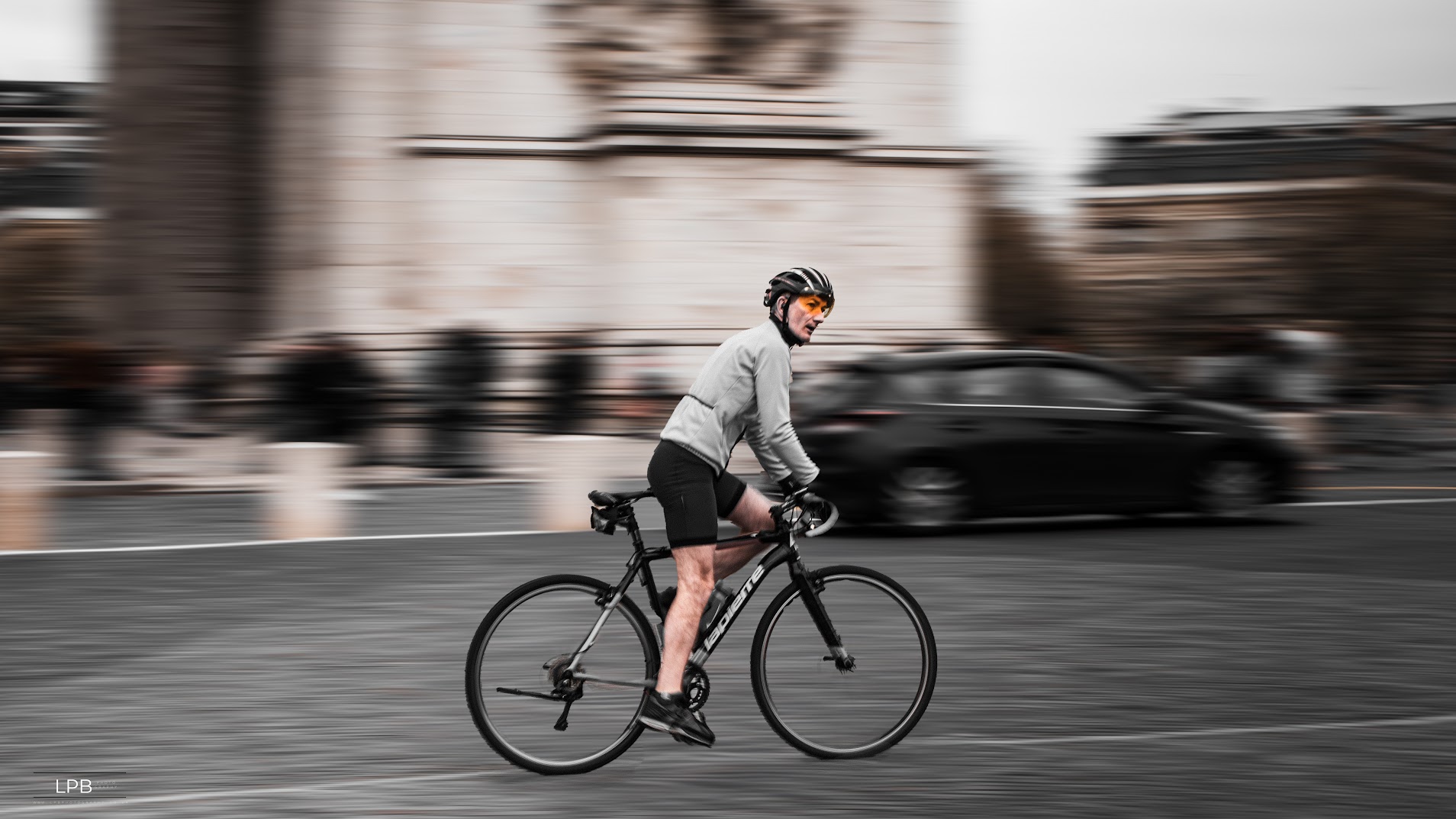 A cyclist sharp against a motion-blurred Arc de Triomphe and passing car